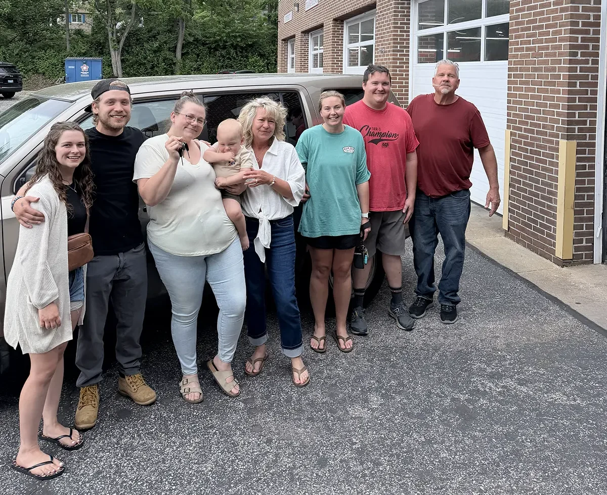 group of people standing next to a car outside an auto repair shop.