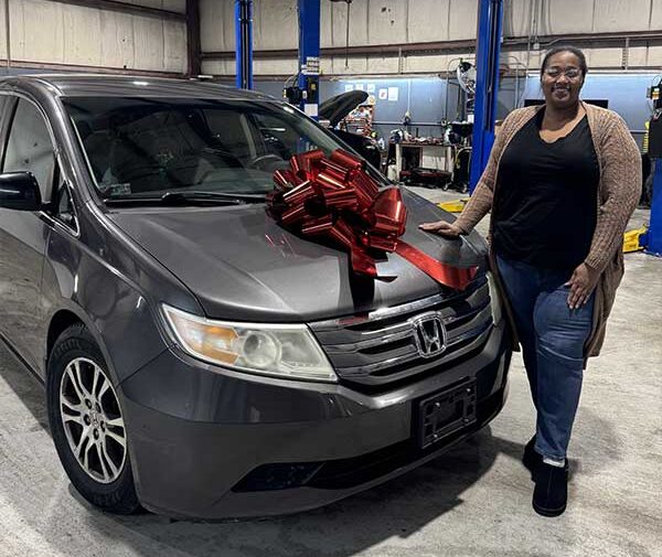Women standing next to white station wagon with red bow on the hood