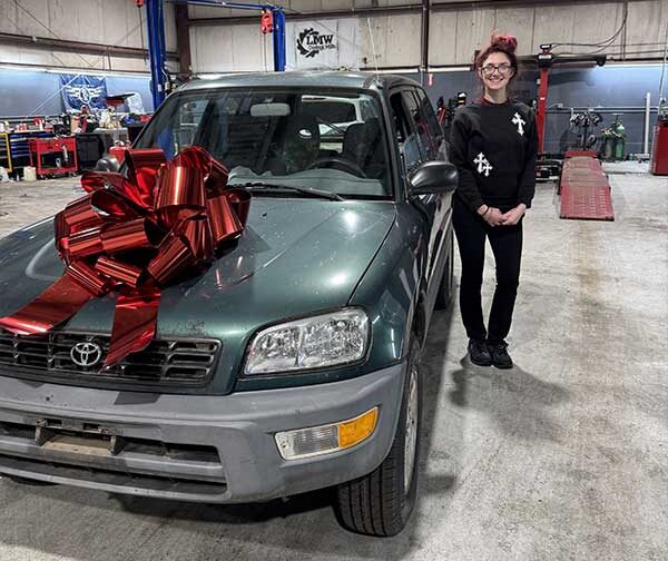 women standing next to white station wagon with red bow on the hood